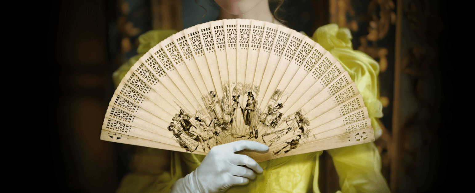 A woman in a yellow period dress holding a fan with illustrations on it 