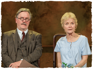 a woman in a blue dress sitting on a chair next to a man in a brown suit