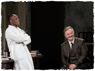 A man in a dark suit sitting on a chair opposite a man in a white coat