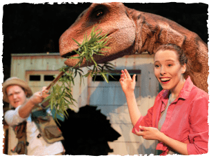 A model dinosaur eating a grassy vine a man is holding onto the other end of as a woman points to them