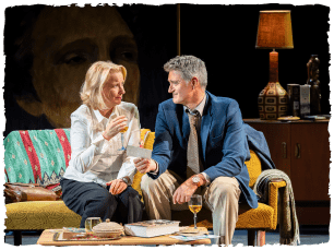 two actors sitting on a sofa talking to each other. 