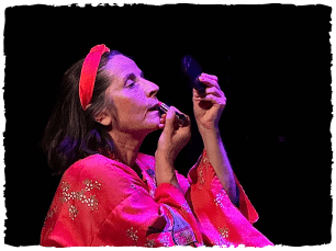 Lady in satin red dressing gown, with matching headband putting on lipstick