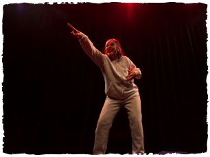 Woman in grey tracksuit, smiling, pointing out to audience with one hand