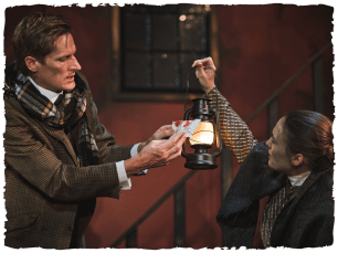 A woman holds up a lamp to a man who is reading a note covered in blood