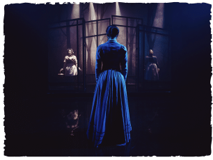 Woman tood on dark stage, with 2 women in front of her
