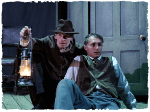 two actors. one kneeling on the floor holding a lamp and one sitting on the floor next to them 