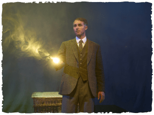 An actor wearing a suit and shining a torch ahead of them
