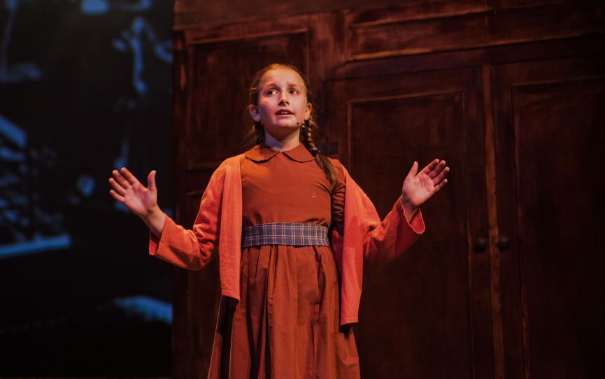 Image of a young girl performing on stage in a red costume.