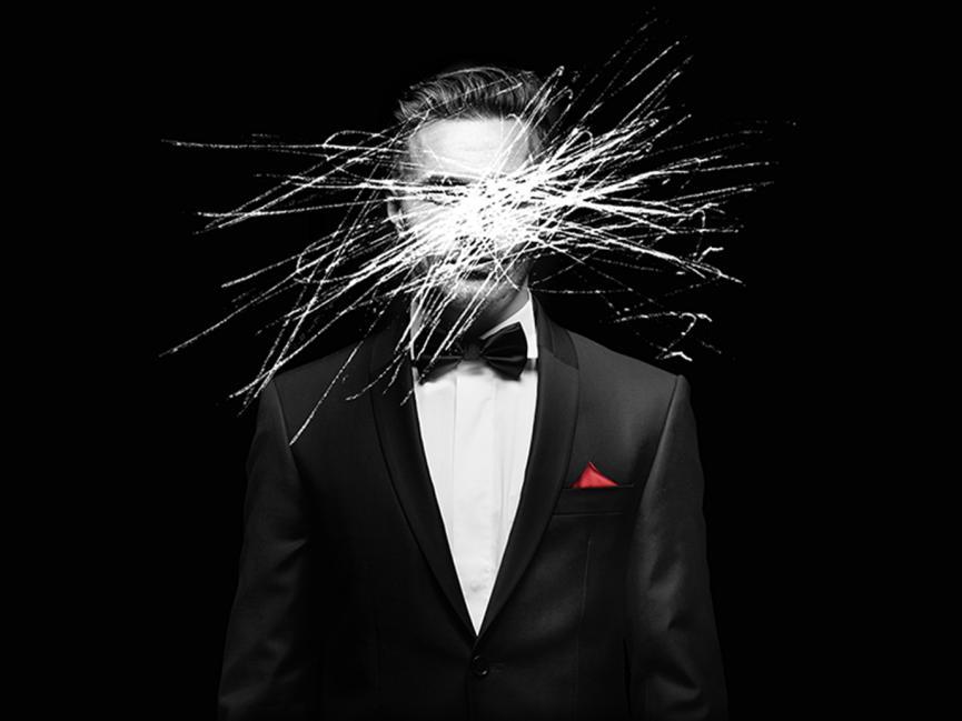 Black background with a man dressed in a tuxedo, with white scribbles over his face.