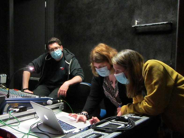 A technician and member of staff from the theatre show a participant from Surrey Choices a piece of software on a laptop backstage.