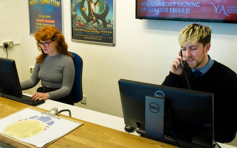 Two members of Box Office staff sat behind computers. One is on the phone while the other looks at the screen.