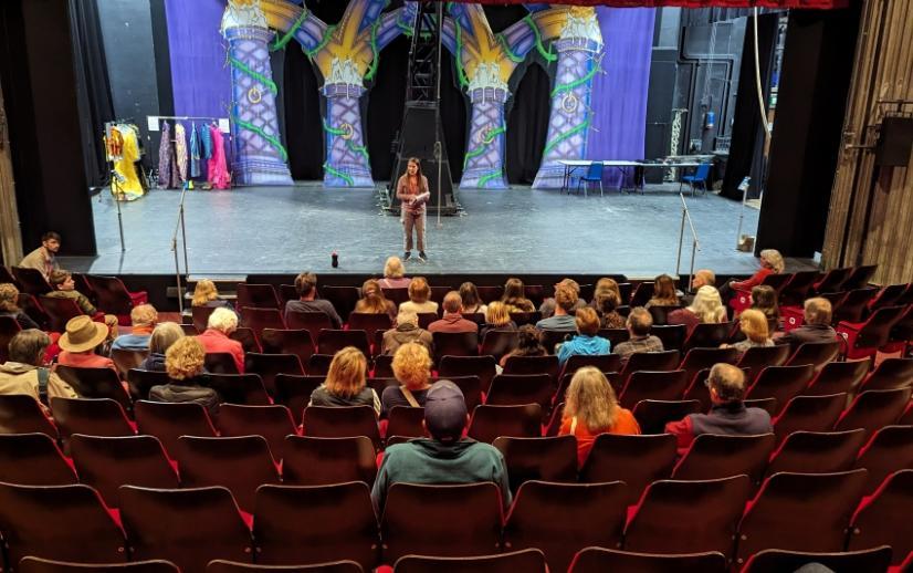 Audience in the theatre auditorium listening to a speaker on the stage with the Panto audience in the background