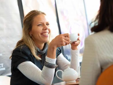 Image shows a woman smiling and holding a coffee cup.