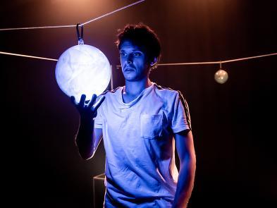 A man stands in a dark room holding a spherical light