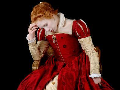 A black background. A woman dressed in a red dress sits on a chair with her head in her hands.