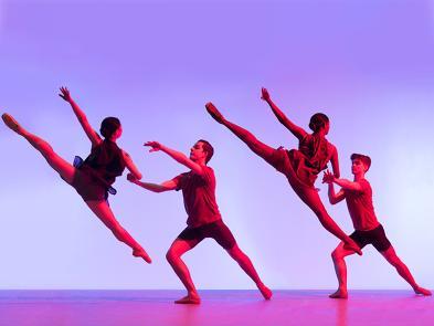 Four dancers in an airbourne pose in front of a purple background.