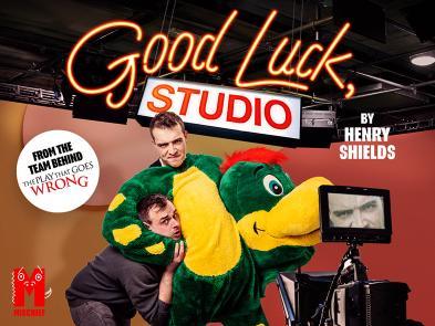A man in a green and yellow dragon costume has another man in a headlock. They are both in a TV studio with the words Good Luck, Studio and 'From the team behind The Play That Goes Wrong' on it.