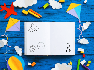 A book containing doodles sits on a blue table adorned with kites, clouds, a plane and a hot air balloon.