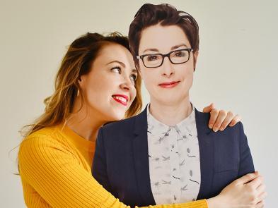 A woman in a yellow jumper hugs a carboard cut out of Sue Perkins