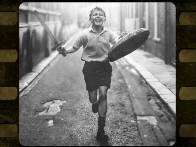 A black and a white image of a young boy running down a street.
