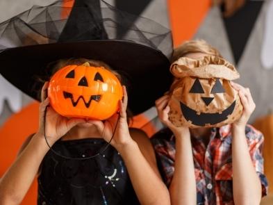 two children in halloween costumes with pumpkins held in front of their faces
