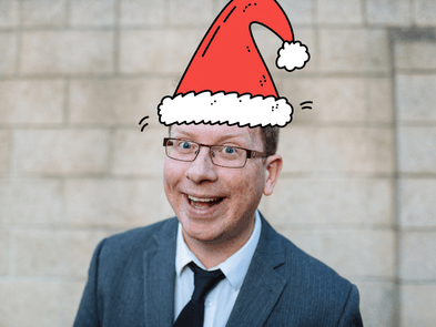 Paul Kerensa, a white male with glasses and brown short hair, is wearing a cartoon Christmas hat and smiling in a jolly way