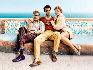 three people sitting on a bench with the sea in the background. The person in the middle has their arms around the two sat either side of them