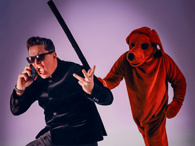 Dom Joly shouting down a phone, with a large red dog behind