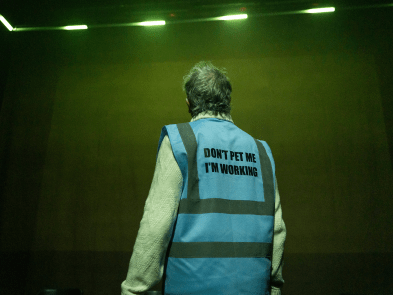 Production shots for The Last Picture - a man turned with his back to the viewer, wearing an assistance dog jacket