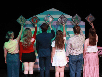 6 actors facing away from the camera holding grad caps