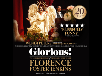 A woman with brown hair and a tiara wearing a pearl necklace and a pink top is singing in front of a pink background with an ornate golden frame, with a smiling man and woman next to her and one woman with her fingers in her ears