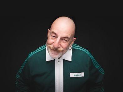 Jeff innocent, white male with bald head moustache, short beard and hoop earring, is wearing a green adidas tracksuit top and facing the viewer with a black background