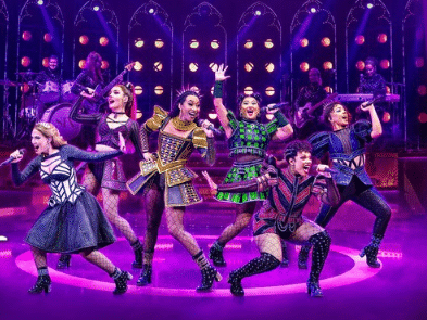 Six actresses wearing colourful outfits singing on stage