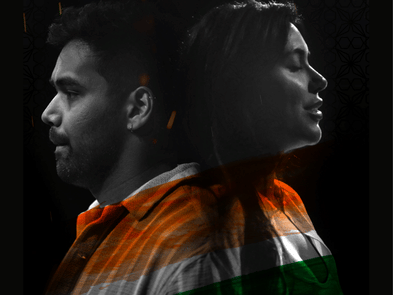 A man and a woman back to back, wearing tops with the colours of the indian flag. Their faces are in black and white against a black background