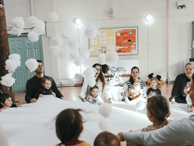 A group of babies and toddlers around a white fabric theyre holding onto